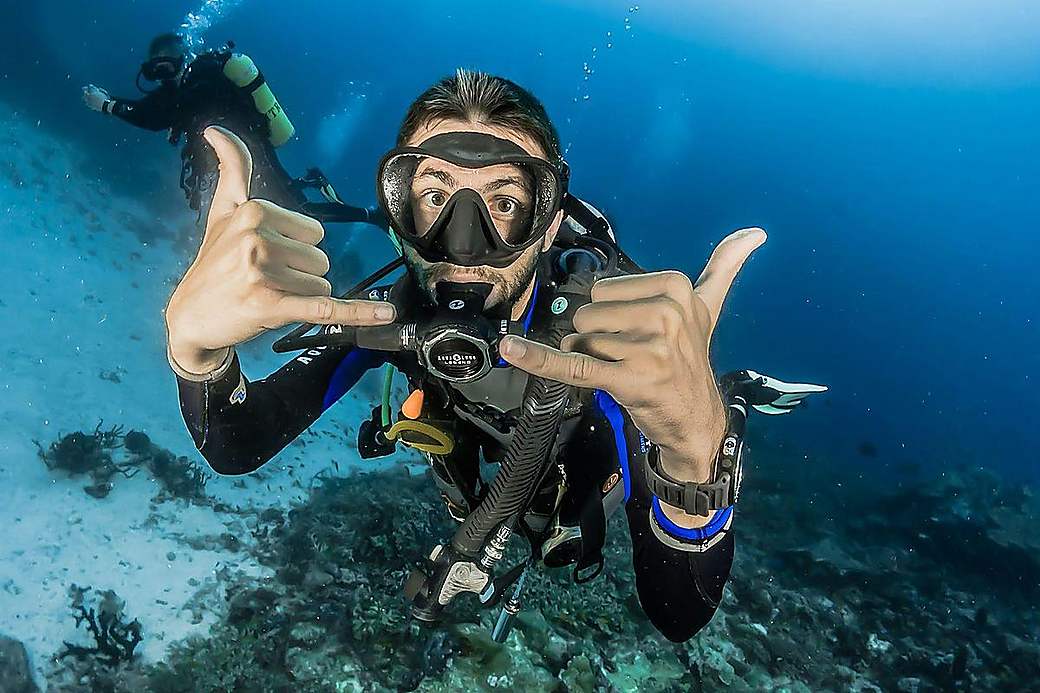 A beginner diver giving the OK sign next to their guide
